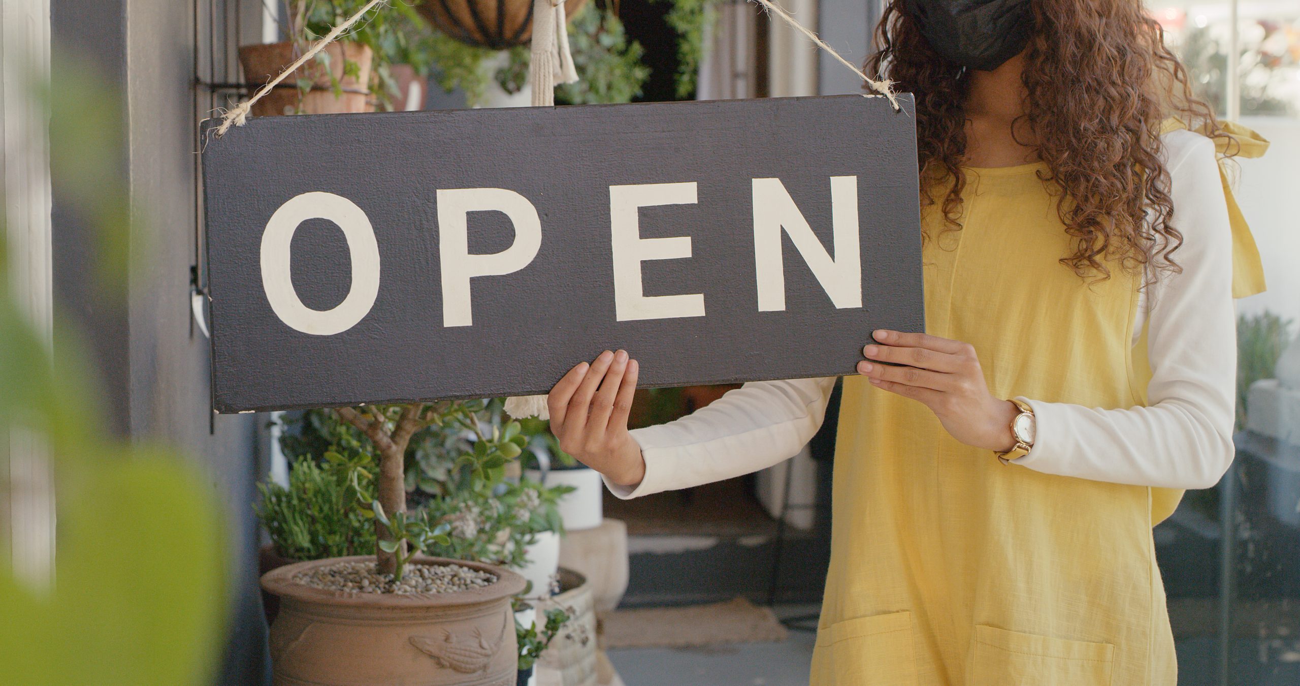 florist holding an open sign in front of business with landscaping in the background increasing business curb appeal